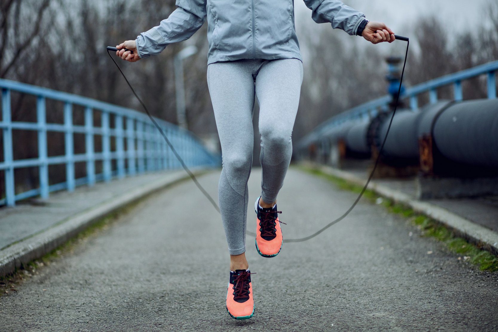 Unrecognizable sportswoman jumping rope on a bridge.